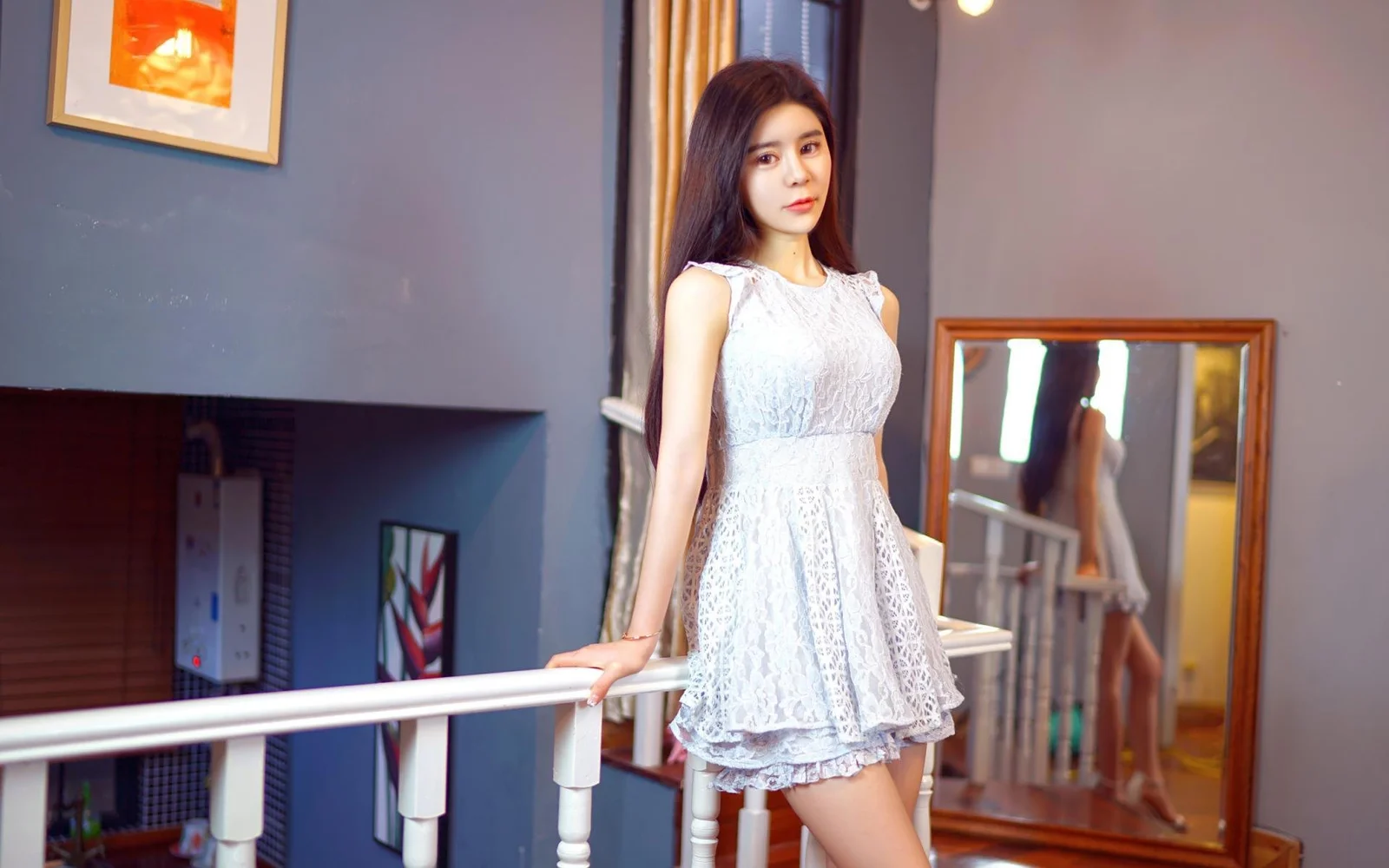 흰색 원피스를 입은 성인 여성이 거울이 있는 실내 난간 옆에 서 있습니다.