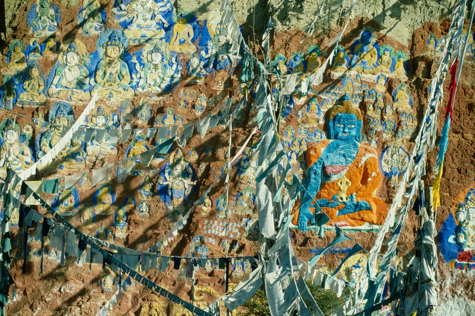 岩壁上绘有色彩鲜艳的佛教人物壁画，前方悬挂着层叠的经幡。