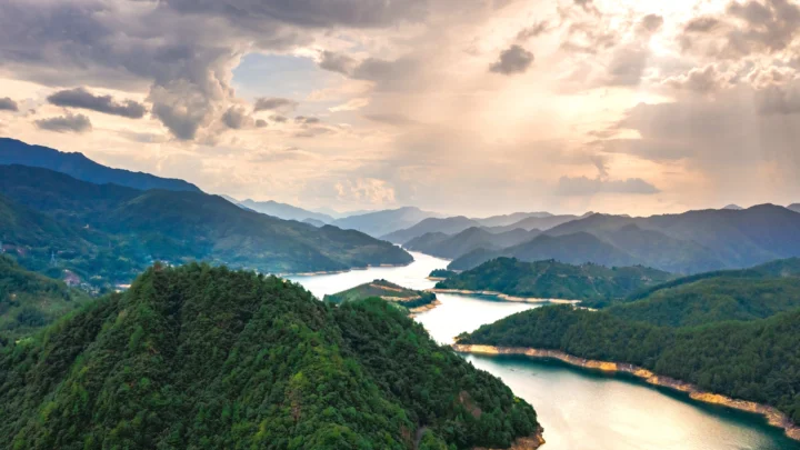 夕阳穿过云层，照亮群山、森林与蜿蜒湖泊。