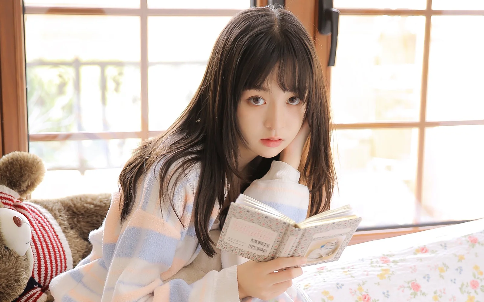明るい窓辺で女性が本を手に読書している。