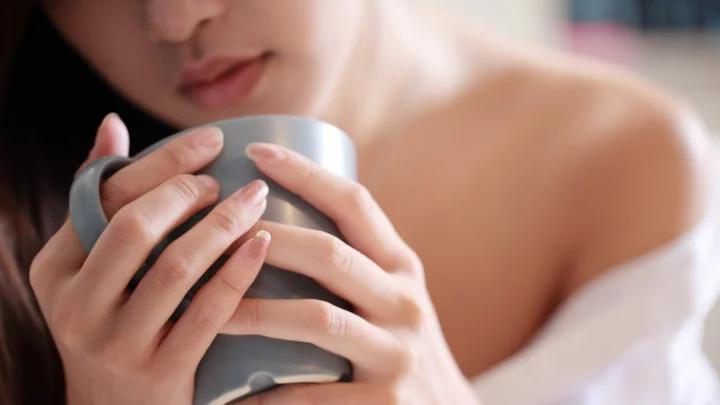 一名女性双手捧着灰色咖啡杯的近距离画面。
