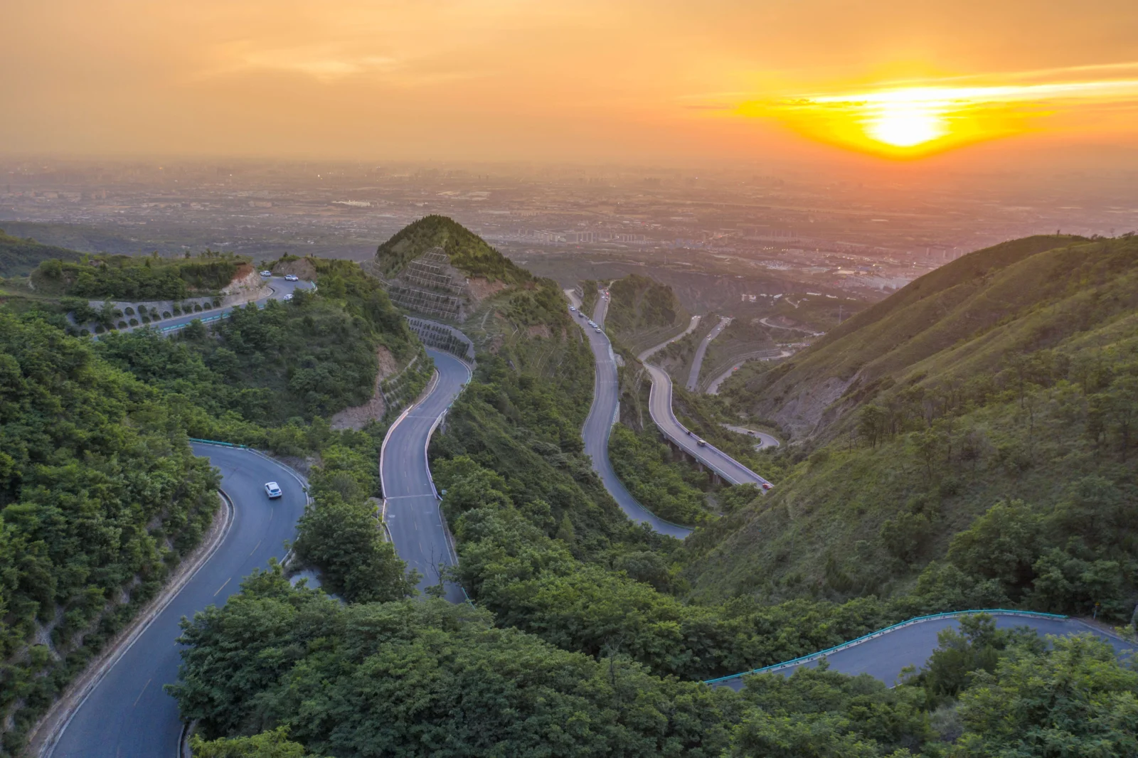 夕阳映照下，骊山绿意覆盖的山坡间蜿蜒着多条公路。