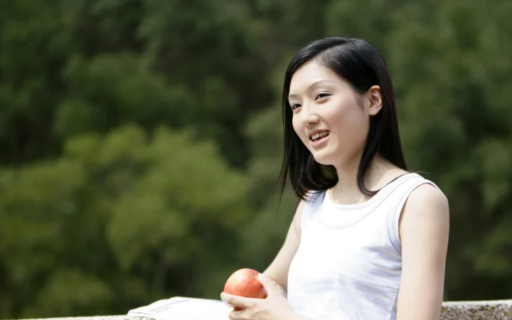 一名黑发女性在树木背景前手持苹果微笑。