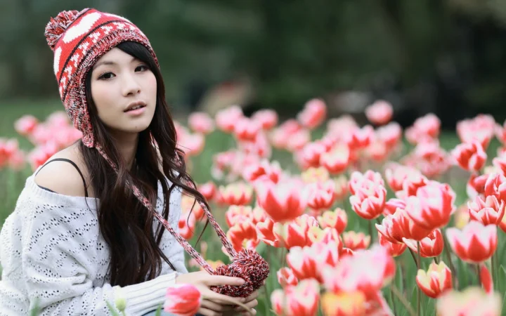 一名戴着红白针织帽的女子坐在盛开的郁金香花田前。