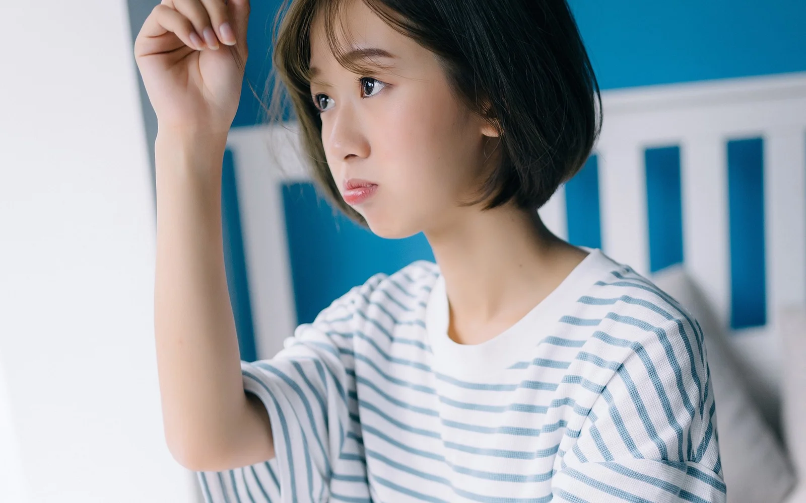 一名短发女性穿着浅色条纹上衣，抬手望向侧前方。