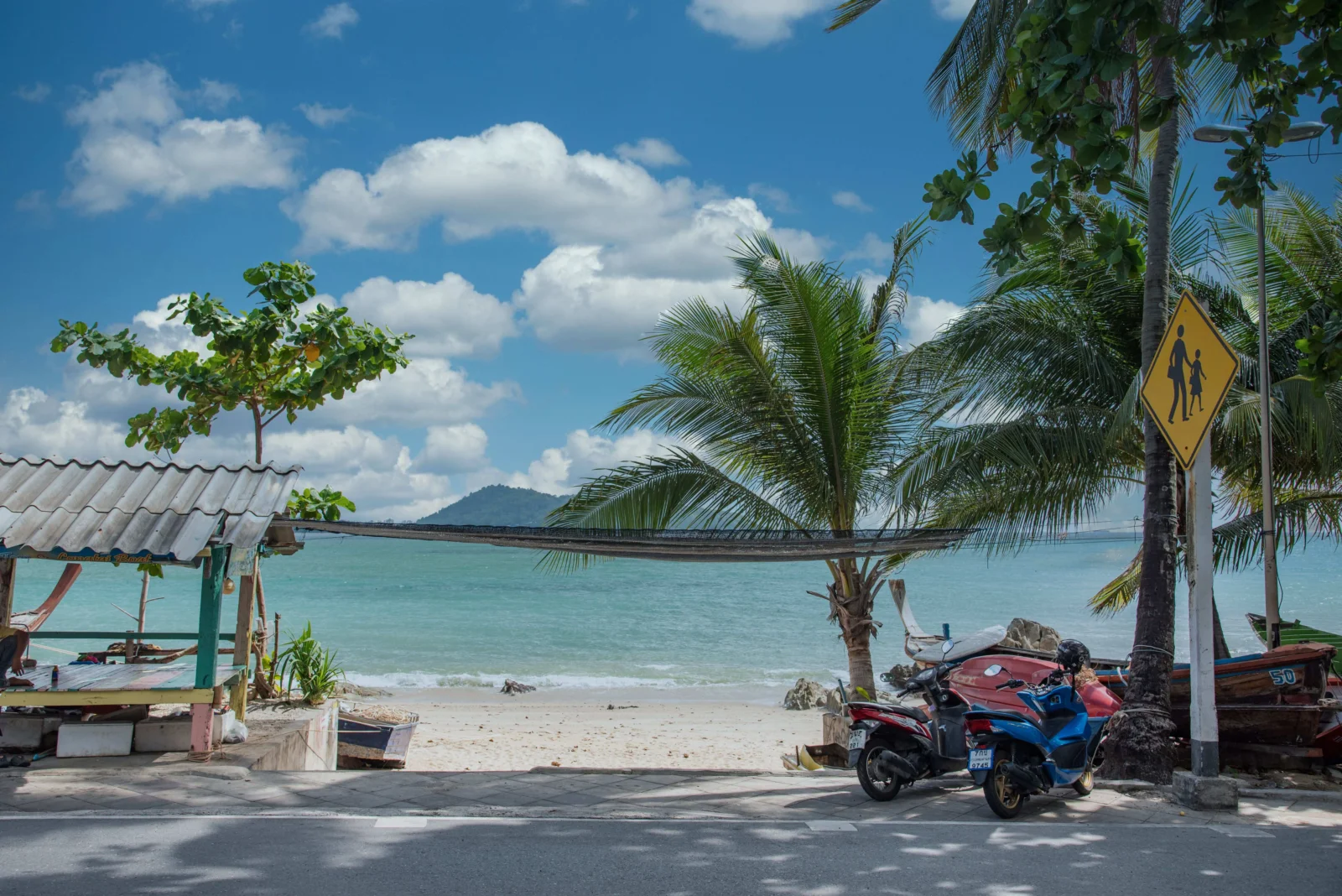 青い海とヤシの木、路肩に停められたバイクが見える tropical beach の風景です。