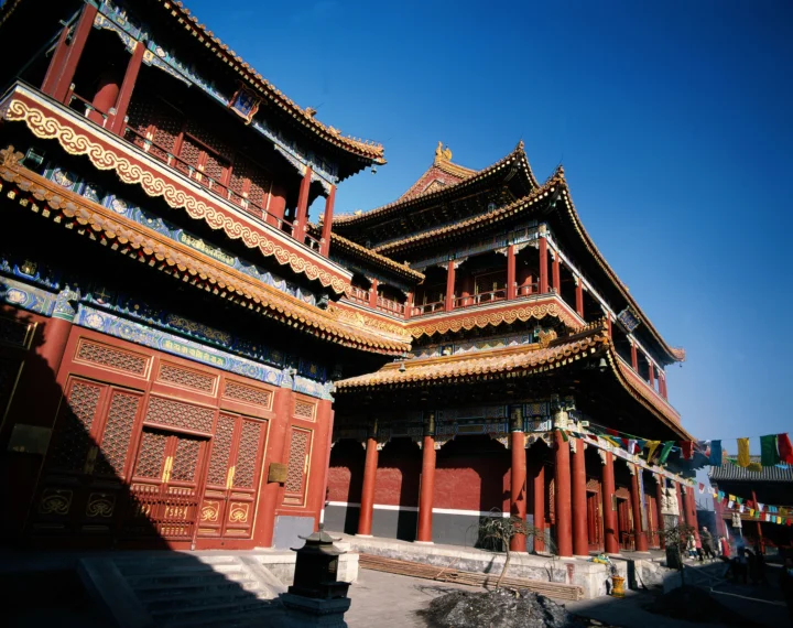 蓝天下，一座红色木结构传统寺庙建筑展现出精美的彩绘装饰和层叠屋檐。