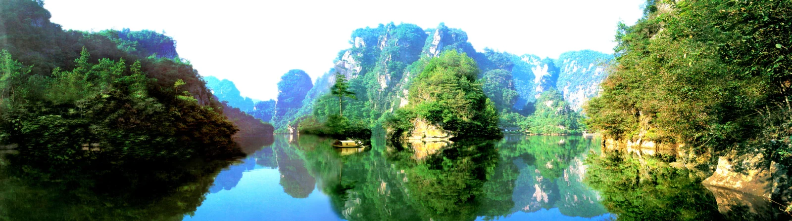 碧绿湖水倒映着森林与高耸山峰，构成一幅宽幅自然风景画面。