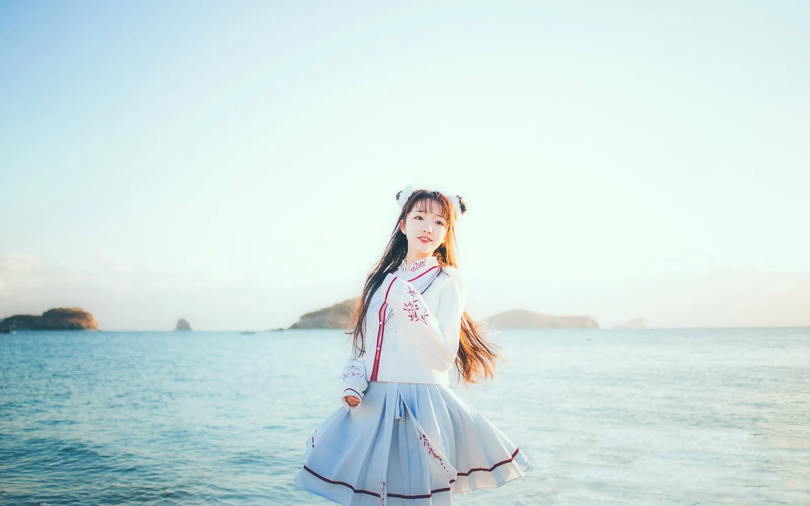 一名身穿浅色连衣裙的女子站在海边，远处可见海岛和开阔海面。