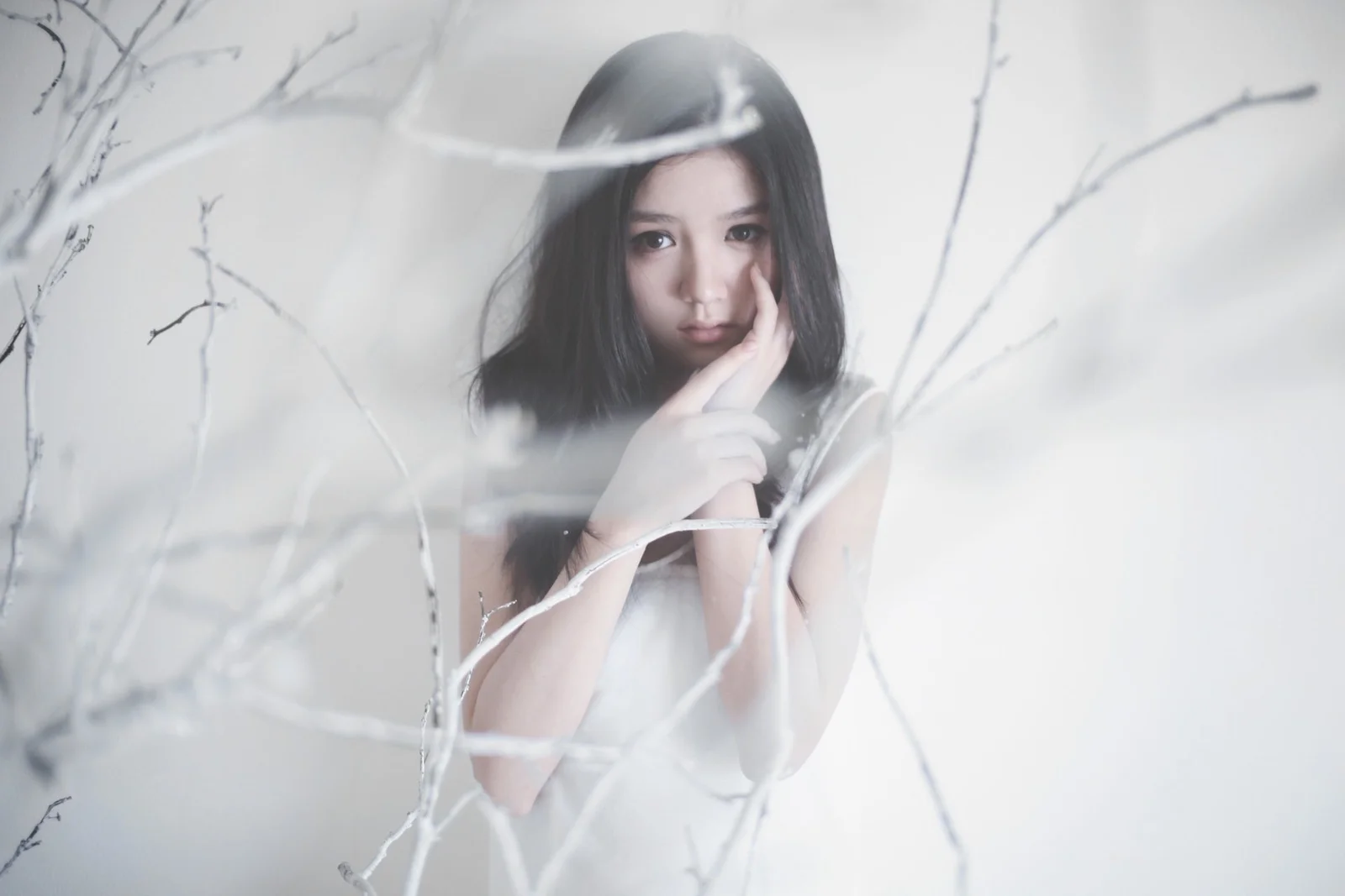 흰 옷을 입은 여성이 흐릿한 흰 가지 사이에 있는 부드럽고 차분한 인물 사진입니다.