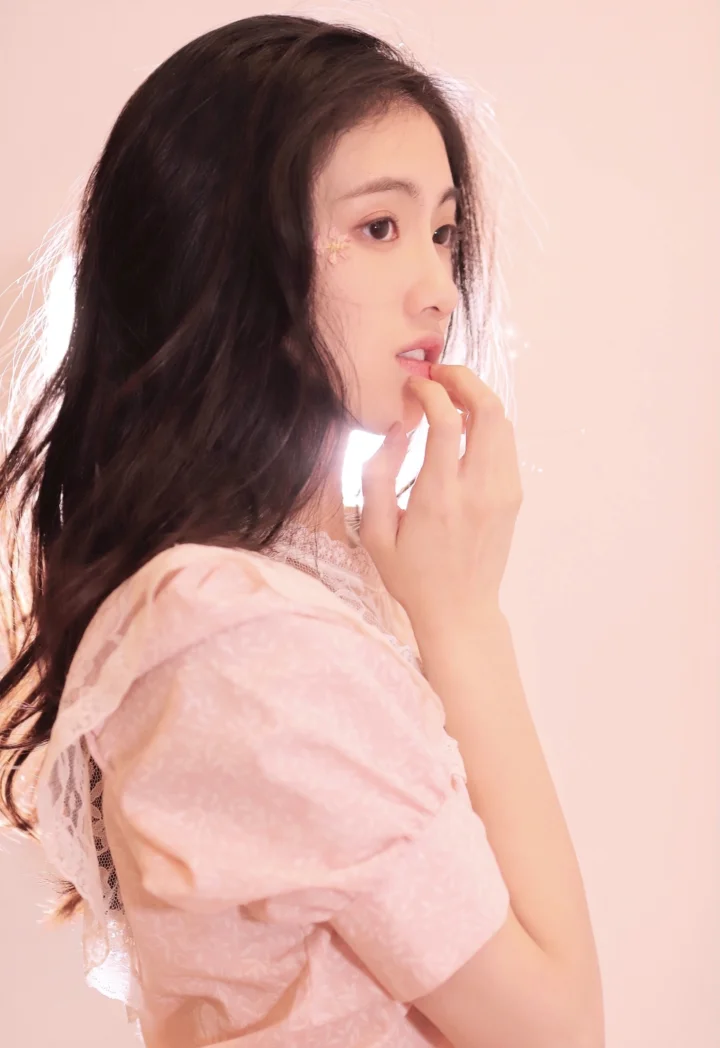 一位身穿粉色上衣的成年女性以侧脸姿态面对柔和的粉色背景。