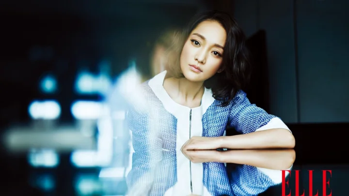 一名成年女性穿着蓝色外套，面向镜头坐在室内光影中。