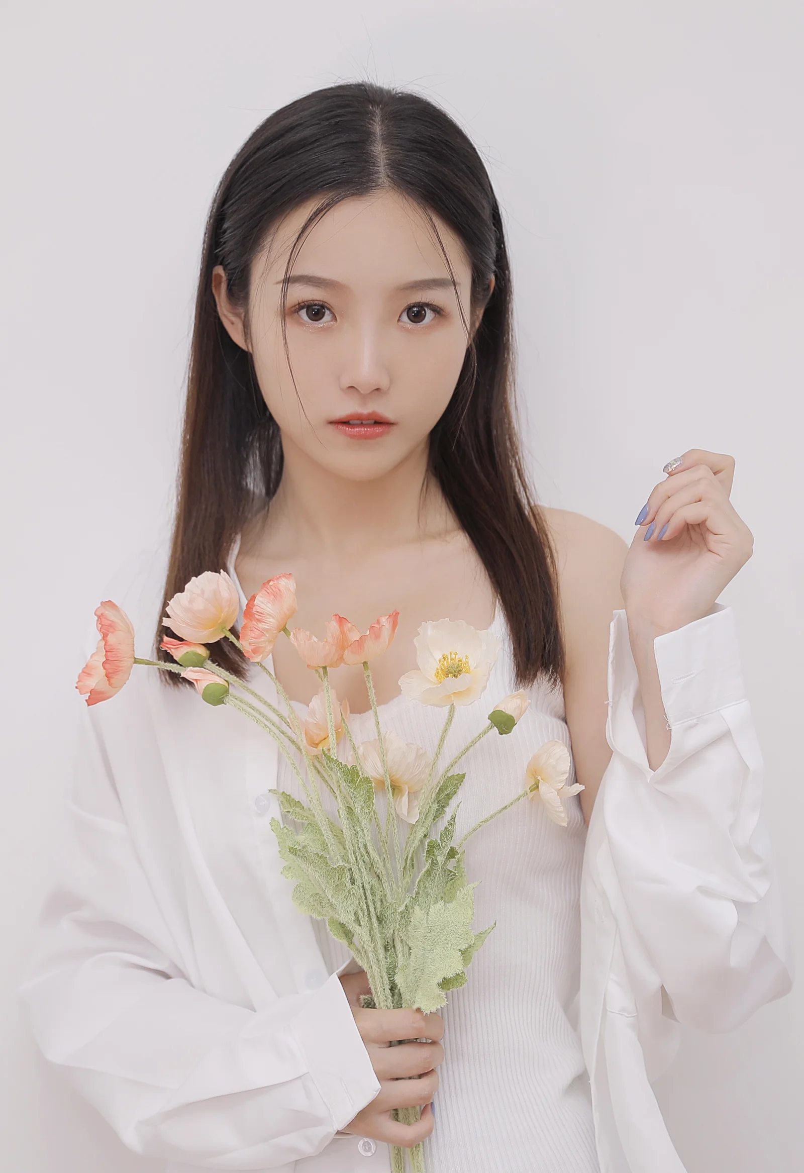 一位长发女性身穿白色服装，手持一束浅色鲜花面对镜头。