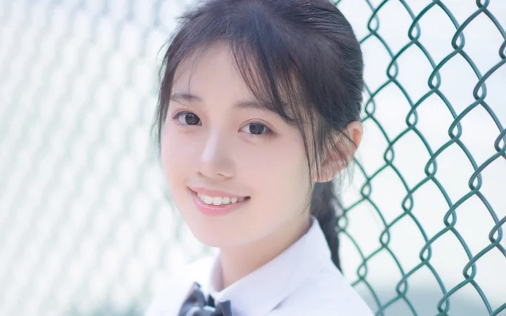 一位面带微笑的女子穿着白色领口服装站在铁丝网围栏旁。