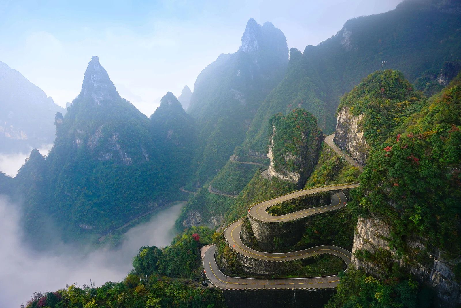 云雾缭绕的群山间，一条盘山公路沿着陡峭的绿色山壁蜿蜒而行。