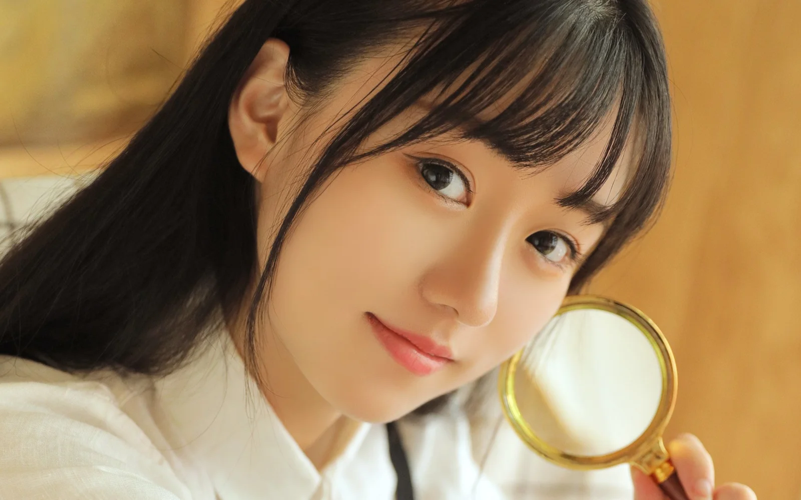 一名黑发女性穿着白色上衣，手持金色放大镜面向镜头。