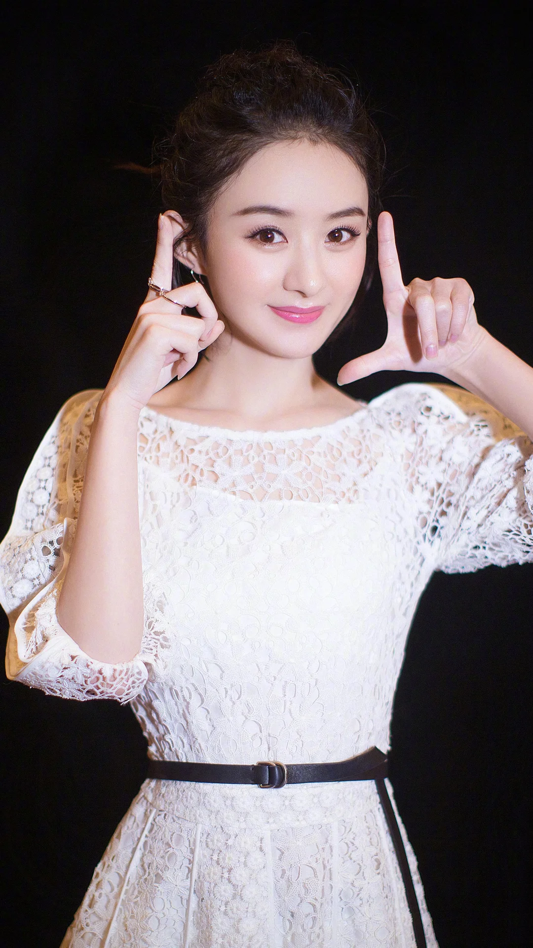 一名成年女性身穿白色蕾絲連身裙，在黑色背景前擺出手勢姿勢。