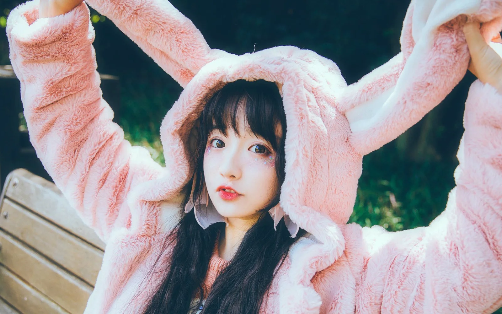 분홍색 토끼 귀 후드티를 입은 여성이 야외에서 양팔을 들고 있습니다.