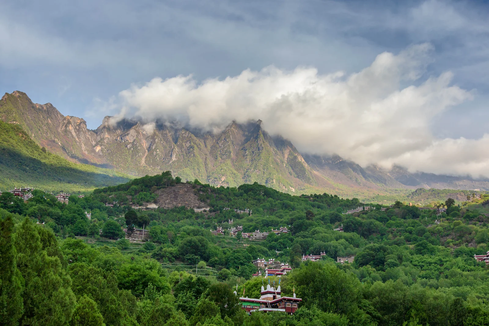 雲に覆われた山々と深い森、谷間の集落が広がる壮大な自然風景。