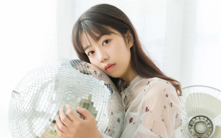 一名成年女性抱着银色镜球，面向镜头坐在明亮的室内。