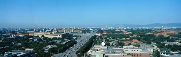 城市全景中，一条宽阔的城市道路穿过成片建筑与绿地，远处延伸至天际线。