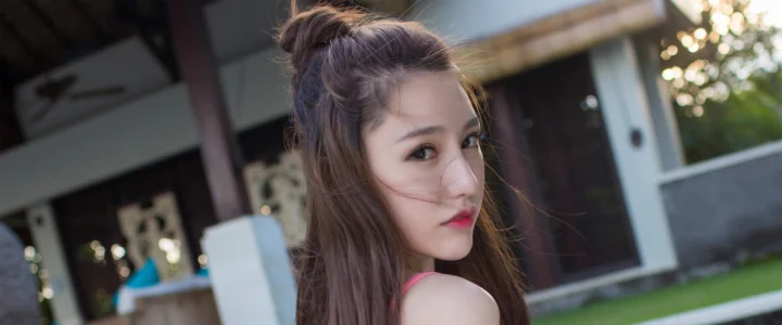 一位长发女性在户外建筑前回望镜头。