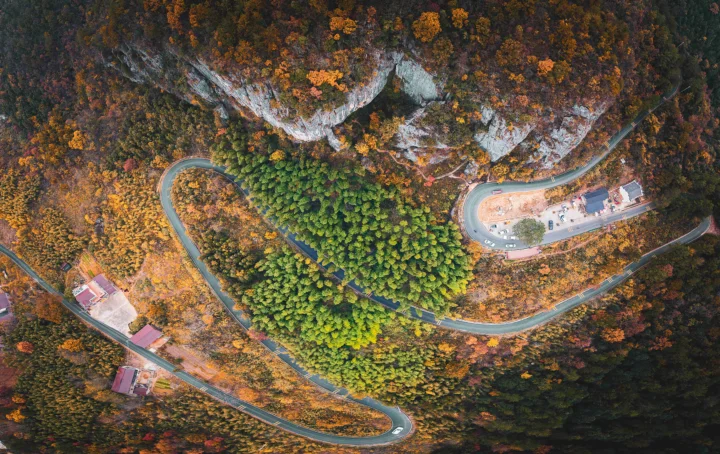 俯瞰视角展现了秋色山林、裸露岩壁和蜿蜒盘山公路。