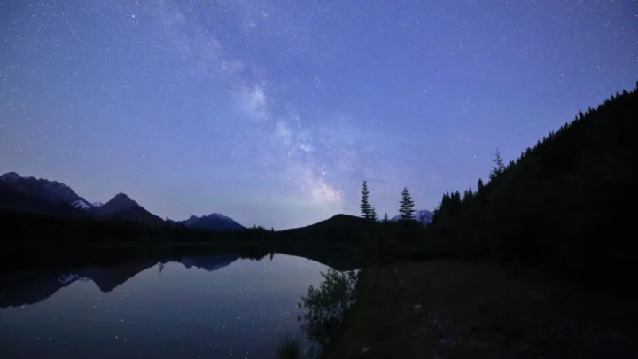 璀璨的银河横跨夜空，群山与宁静湖面形成深色剪影和倒影。