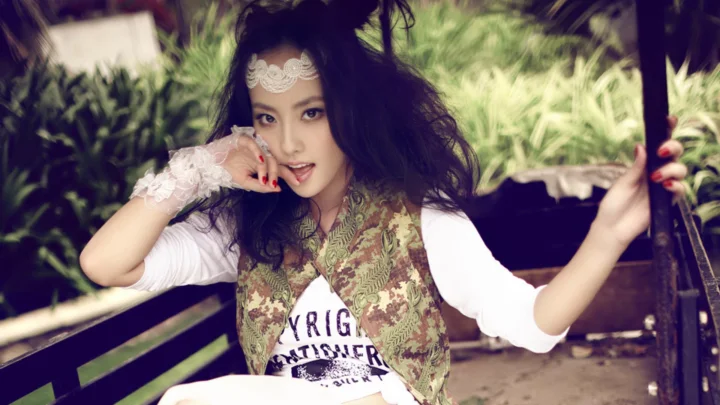 一名成年女性坐在户外木结构旁，身穿印花马甲和白色上衣。