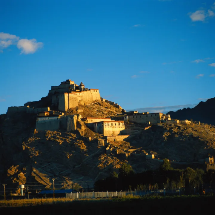 夕阳照亮了坐落在岩石山丘上的古老堡垒，背景是湛蓝天空。