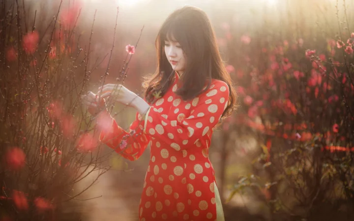 一名身穿红色圆点连衣裙的女子站在盛开的花枝间。