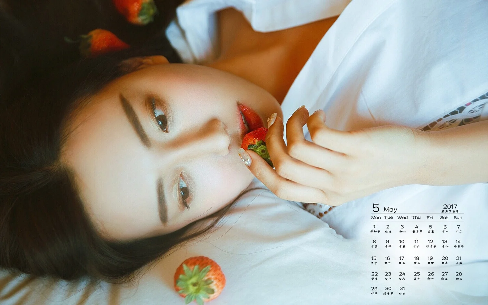 一名成年女性躺在床上手拿草莓，画面下方带有日历。