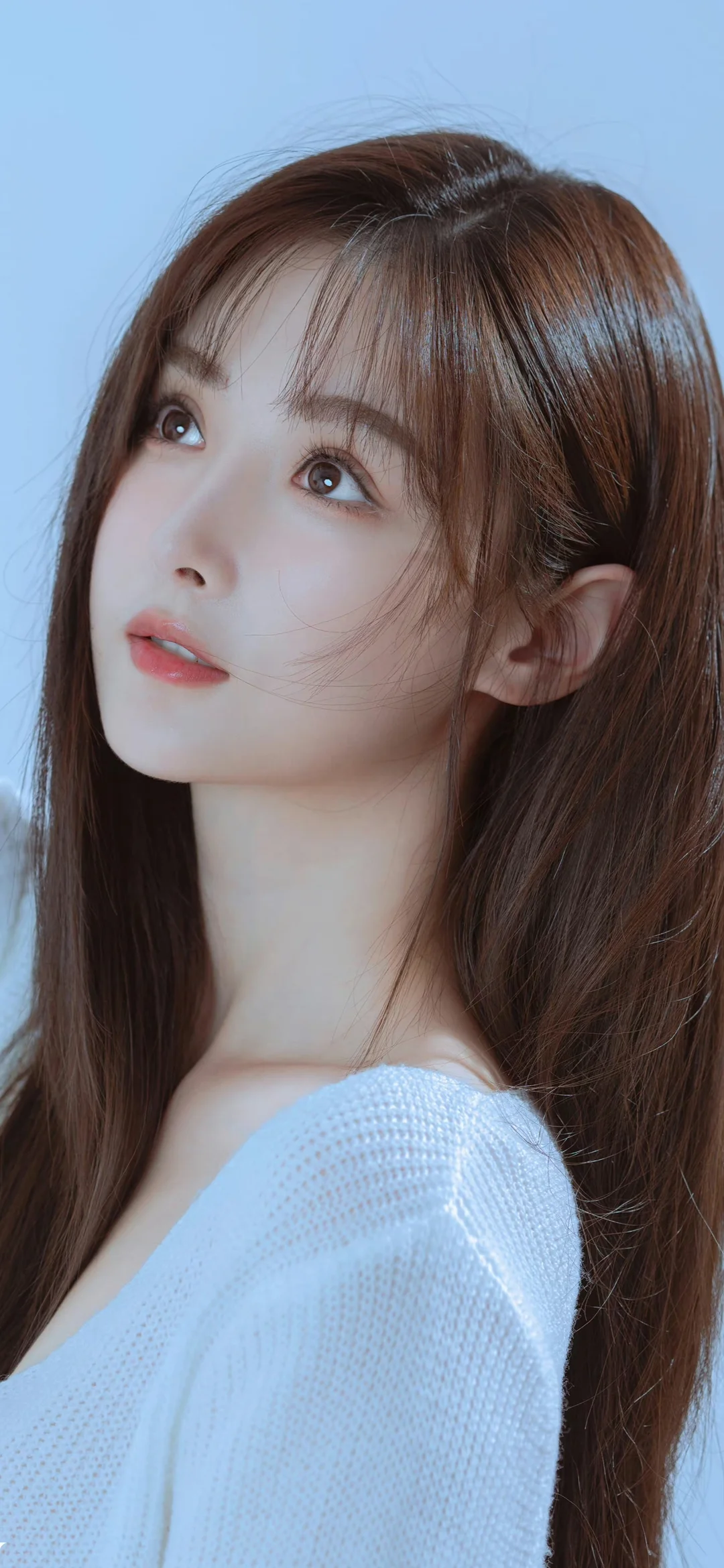 一名长发女性身穿浅色针织衫，在蓝色背景前侧脸抬头注视。