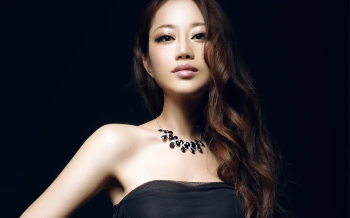 一位长发女性身穿黑色无肩带上衣，佩戴项链，在深色背景前进行棚拍人像摄影。