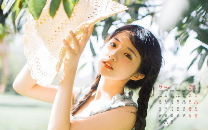 一名成年女子在树叶环绕的户外阳光下举起浅色镂空织物，右下角叠有日历。