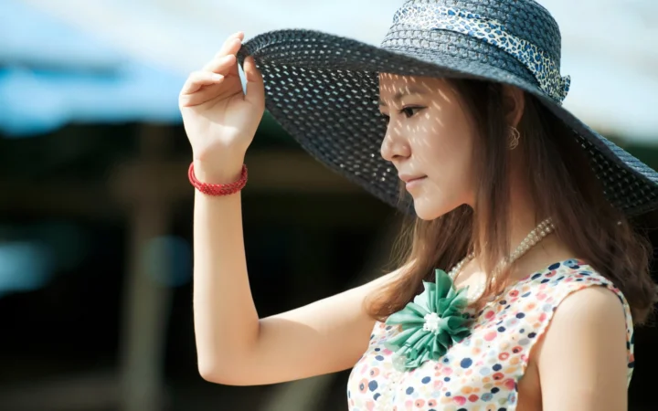 一名戴着宽檐帽、身穿彩色无袖上衣的成年女性在户外侧身望向一侧。