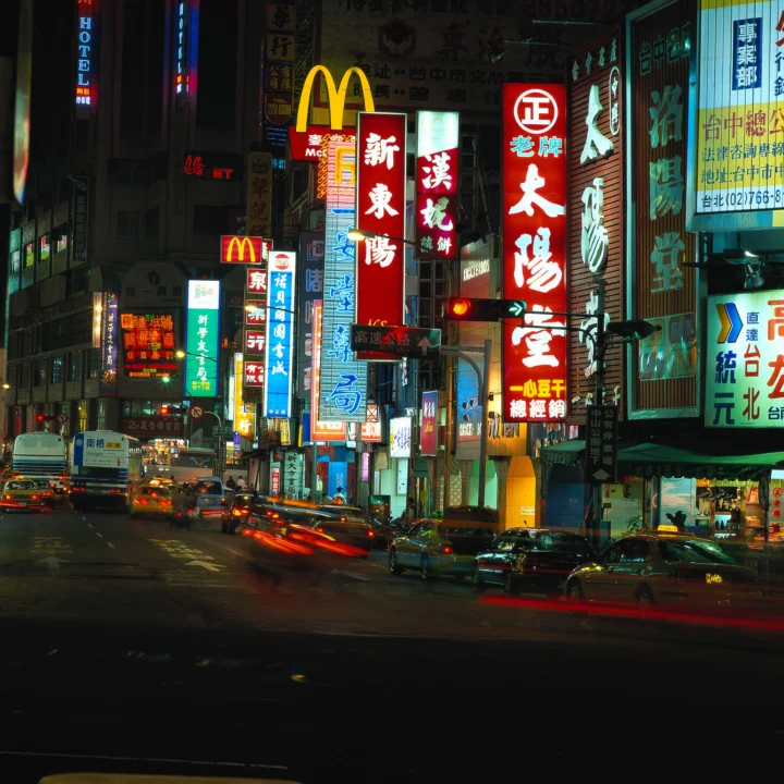 夜晚繁华街道两旁布满霓虹招牌，车辆在街面上流动。