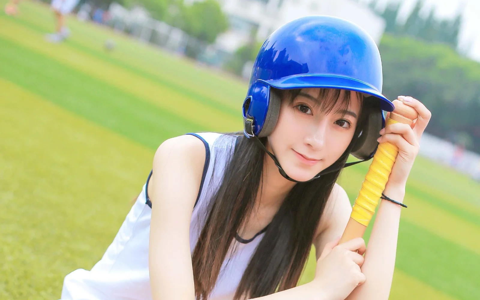 一名戴著藍色頭盔的女性在草地上手持球棒。