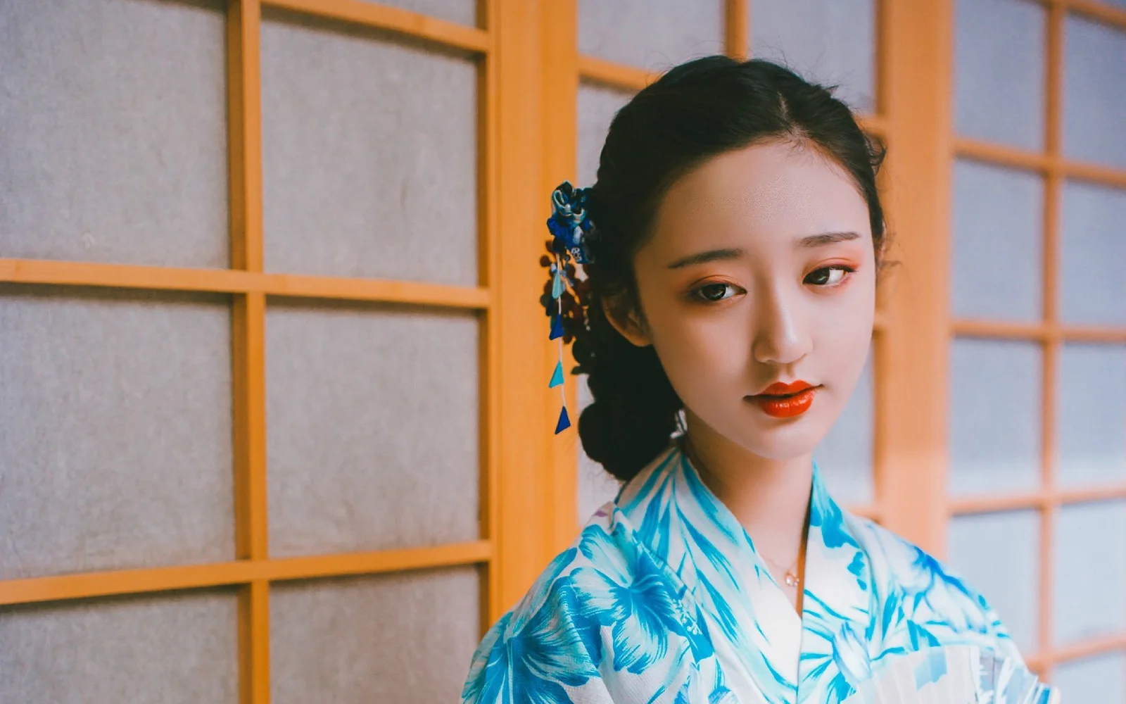 青い伝統衣装を着た女性が木製の格子窓の前に立っています。