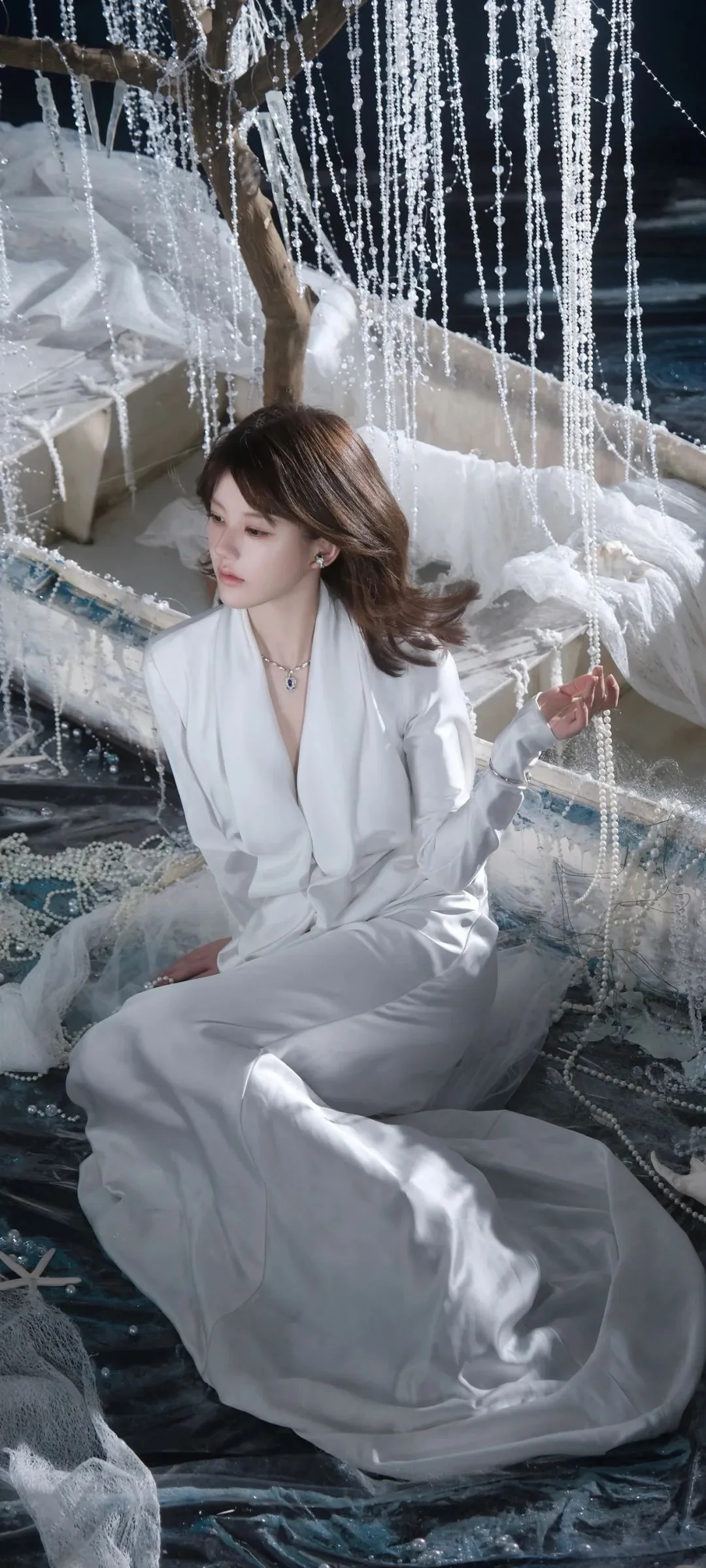 一名身穿白色服装的女性坐在垂挂的珠串装饰前。
