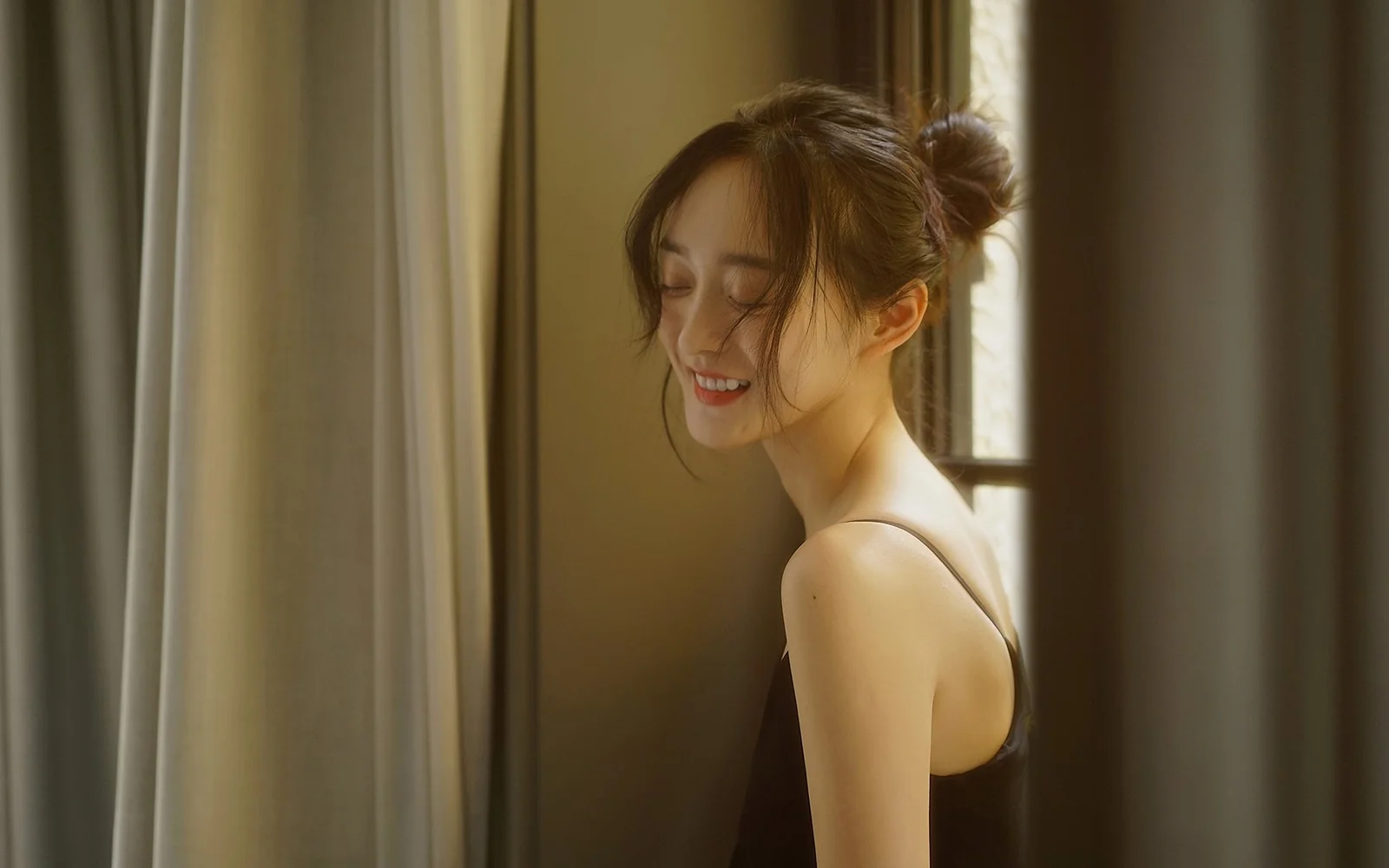 一名女性站在窗边和窗帘之间，沐浴在温暖的光线中。