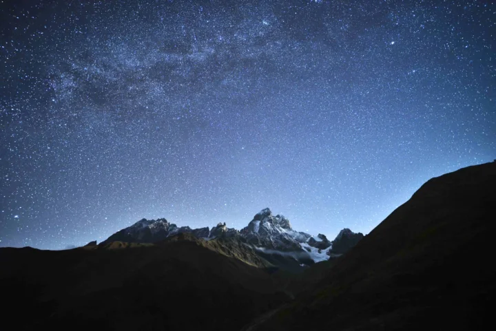 繁星密布的夜空下，深色山谷中耸立着覆雪的群山。