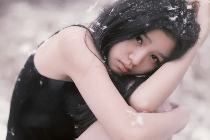 一名黑发女性以手臂支撑头部，面向镜头呈现柔和的肖像画面。