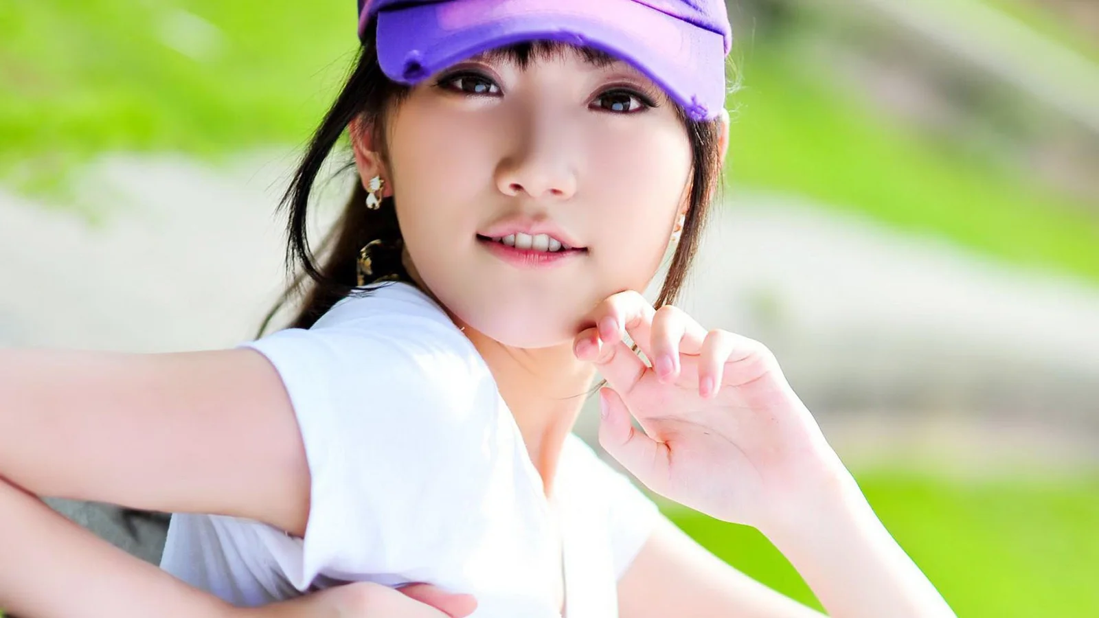 一名戴紫色帽子、穿白色上衣的女性在明亮的绿色户外背景前微笑。