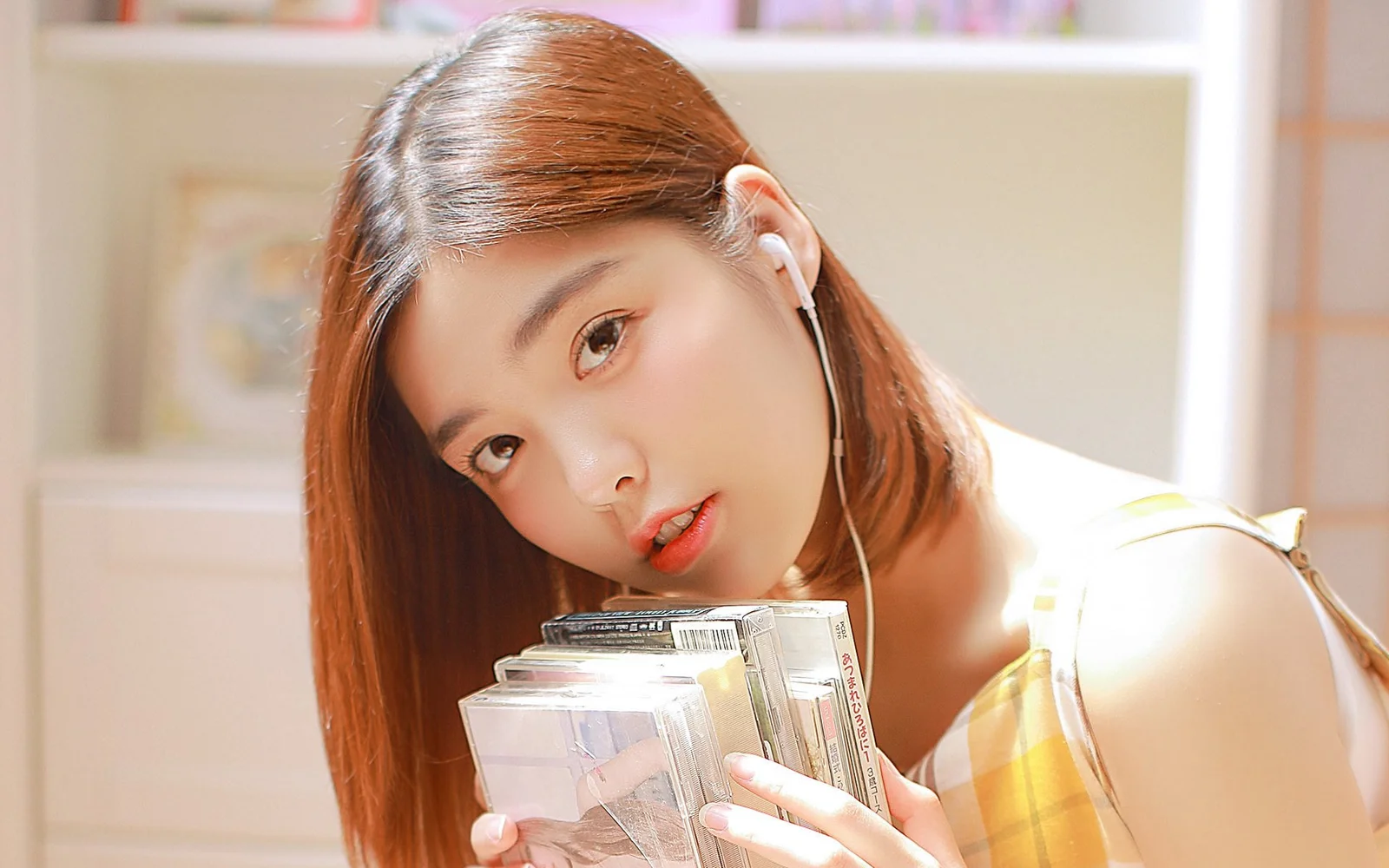 一名成年女性在室内阳光下手捧书籍并佩戴有线耳机。
