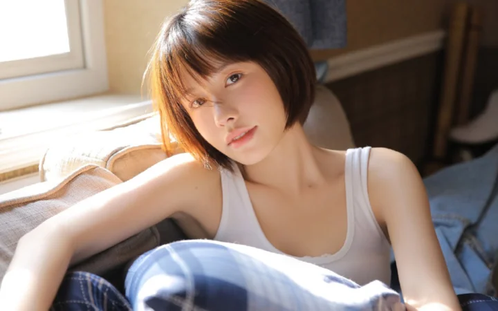 一名成年女性坐在沙发上，沐浴在窗边的阳光中。
