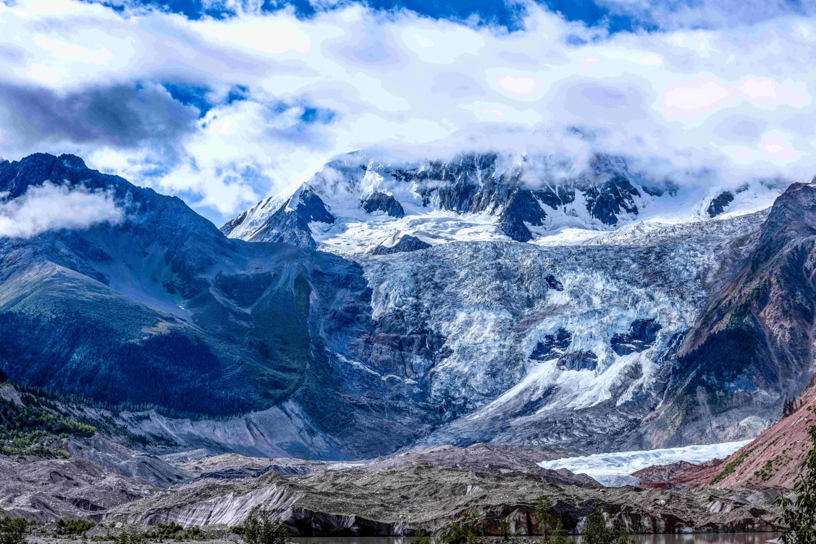 壮丽的雪山冰川在云层下延展开来，前景可见少量湖水。