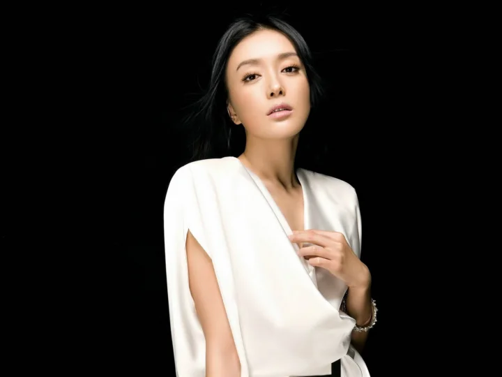 검은 배경 앞에 흰색 블라우스를 입은 성인 여성이 서 있습니다.