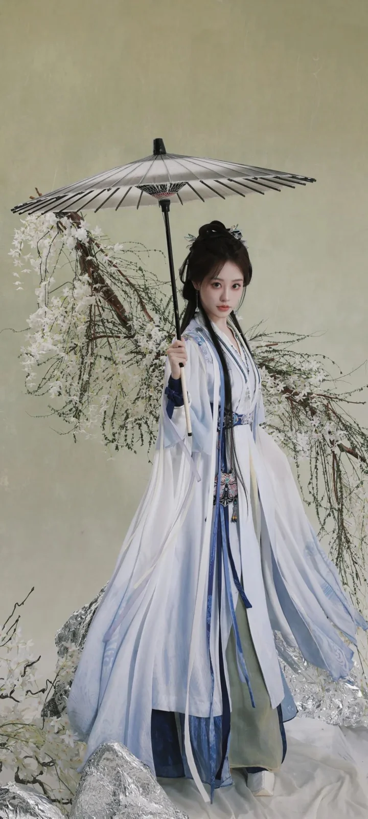 伝統衣装の女性が花枝を背景に和傘を差して立っている。