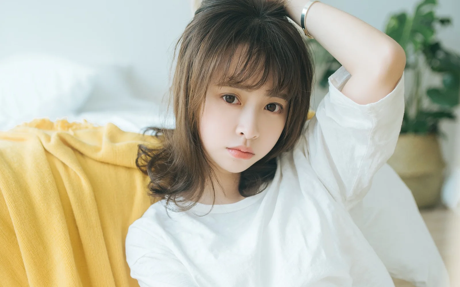 一名女性在室内沙发旁抬手整理头发并看向镜头。